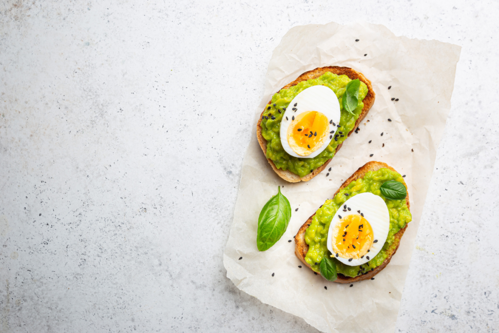 Avocado egg toast topped with sliced boiled egg and fresh basil