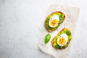 Avocado egg toast topped with sliced boiled egg and fresh basil