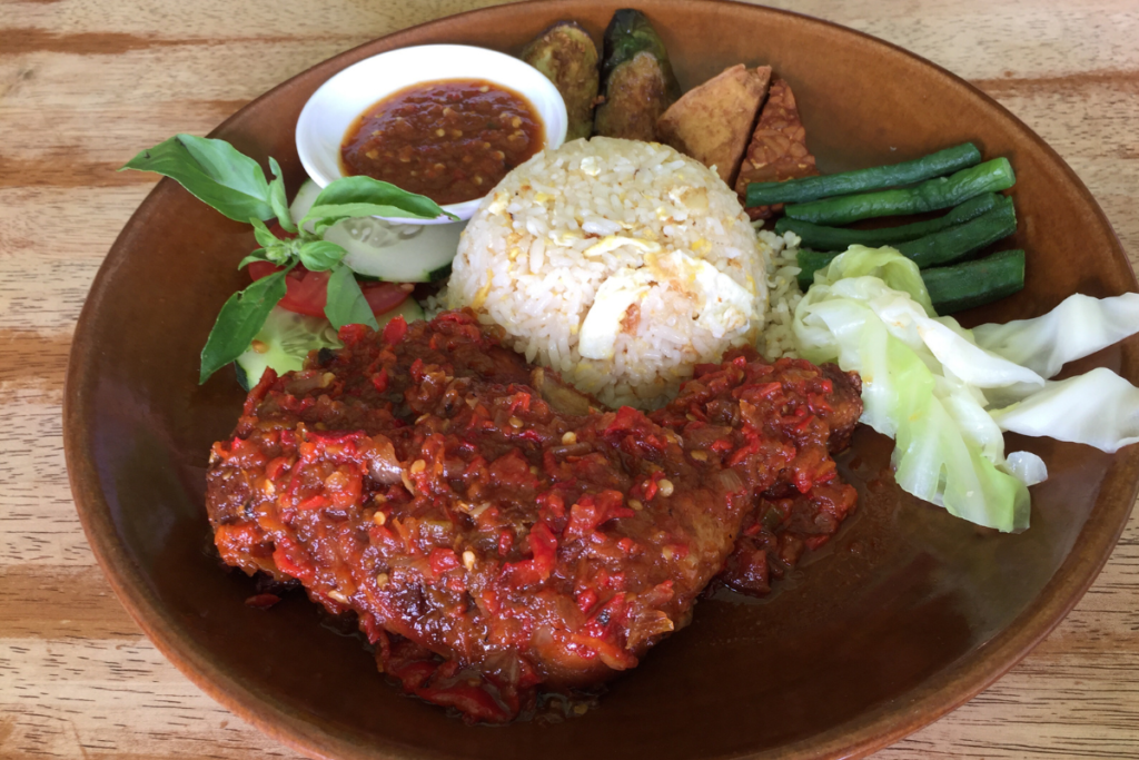 Healthy Ayam Penyet served with white rice, fresh sambal, vegetables, tofu and tempeh on a wooden plate.