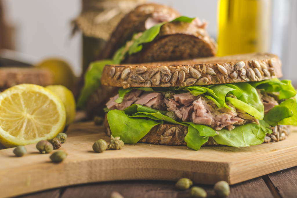 A healthy wholegrain sandwich filled with tuna and fresh leafy greens, served as a balanced meal.