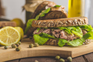 A healthy wholegrain sandwich filled with tuna and fresh leafy greens, served as a balanced meal.