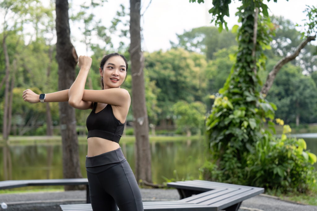A woman performing upper body stretching exercises outdoors before a workout in a peaceful park.