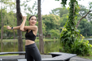 A woman performing upper body stretching exercises outdoors before a workout in a peaceful park.