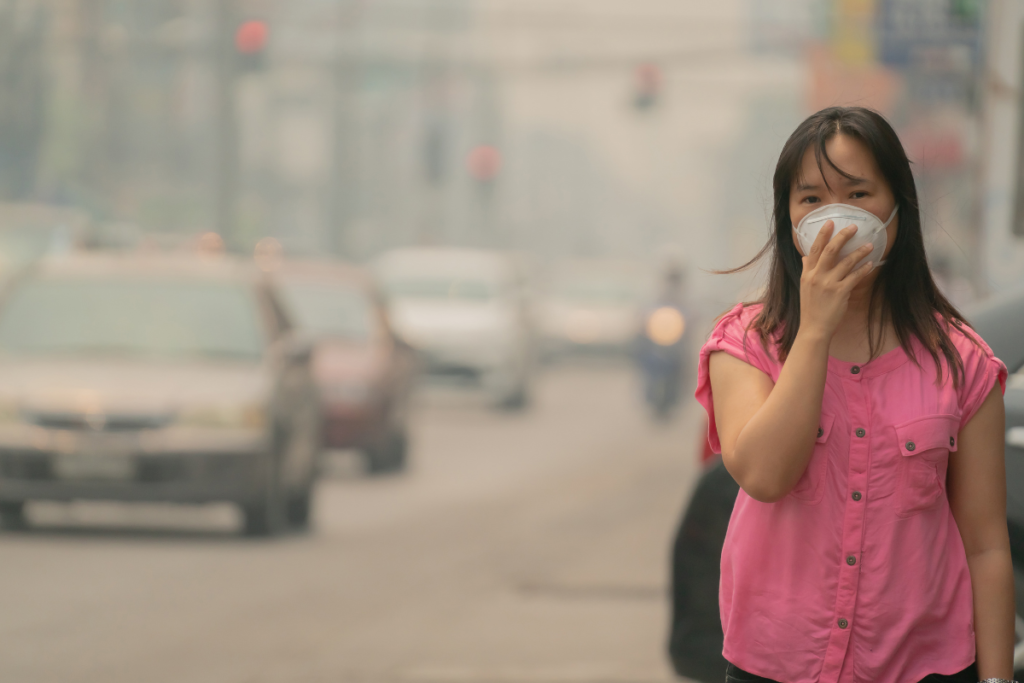 Woman wearing a face mask outdoors on a hazy, polluted city street.