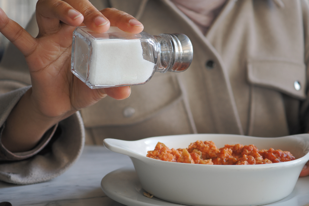 Person adding salt to a meal at the dining table.