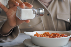 Person adding salt to a meal at the dining table.
