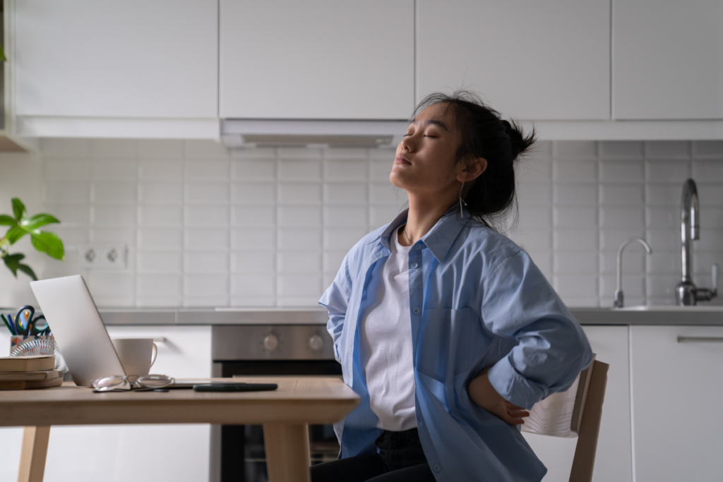 Woman experiencing lower back pain while sitting at a desk with a laptop.