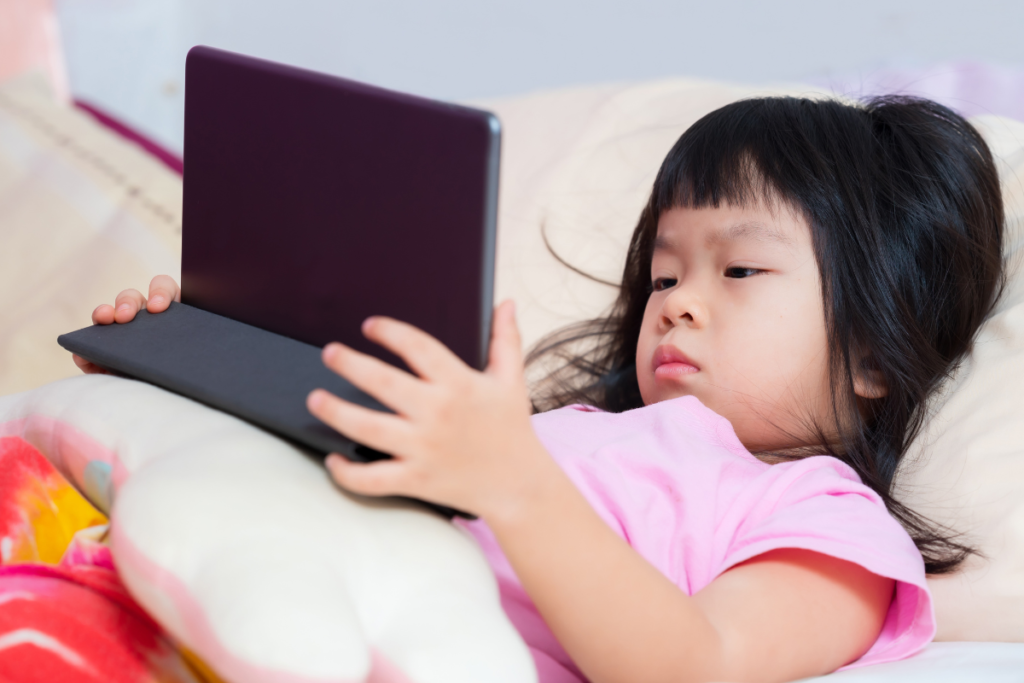 Young child using a tablet while lying in bed.