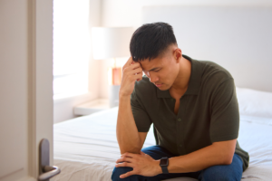 Man sitting alone on a bed appearing distressed and emotionally overwhelmed