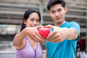 Active man and woman holding a red heart together after exercising.
