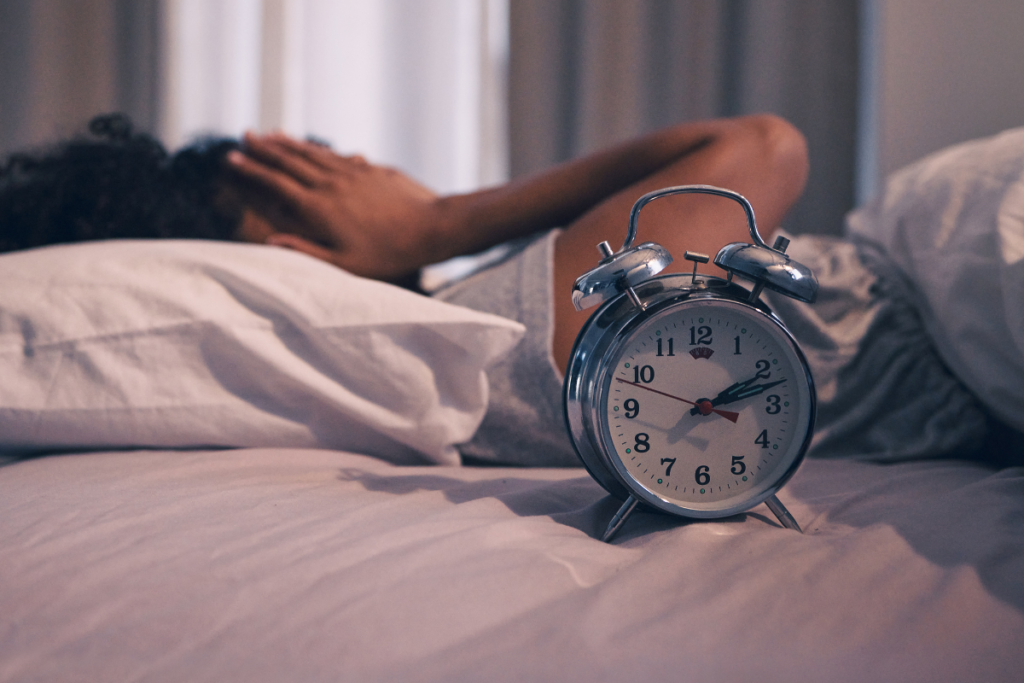 Person lying awake in bed beside an alarm clock while struggling to sleep.